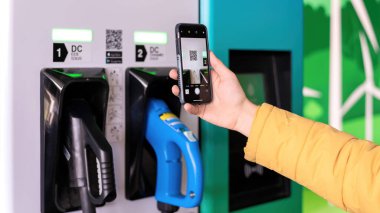 CHISINAU, MOLDOVA - 26 Nisan 2021: Bir adam akıllı telefonuyla elektro arabanın şarj cihazında qr kodunu tarıyor