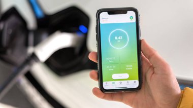 CHISINAU, MOLDOVA - 26 Nisan 2021: Adam elektro arabayı şarj ediyor, akıllı telefonu işlem durumuyla şarj ediyor