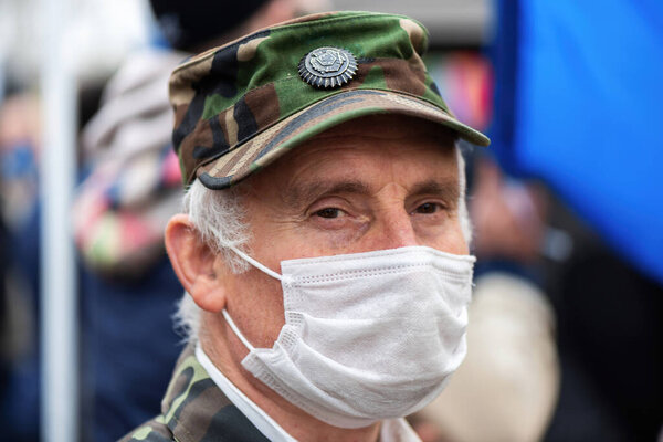 CHISINAU, MOLDOVA - APRIL 28, 2021: An old man in military suit and medical mask looking into camera, people protesting for snap elections in front of constitutional court building