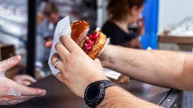Client's hand holding finished burger in a paper cover, food truck. Street Food