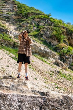 Kıvırcık saçlı genç bir adam kamerayla çekim yapıyor, kayalık bir tepede kalıyor.