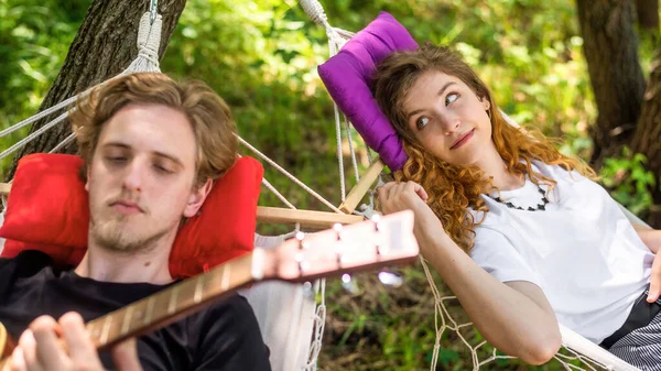 ハンモックの上に寝そべっているカップル 女性が彼を見ている間若い男がギターを弾いている 緑の周り グラミング — ストック写真