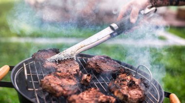 Izgarada et kızartan bir adam. Çevrede yeşillik. Glamping