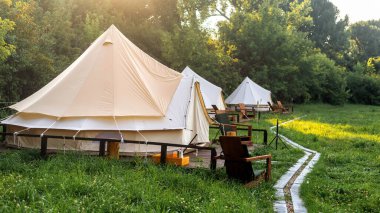 Glamping, birkaç çadır, ön planda sandalyeler ve patika.