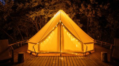 Geceleri glamping, önünde sandalyeler olan parlayan çadır, gece lambaları.