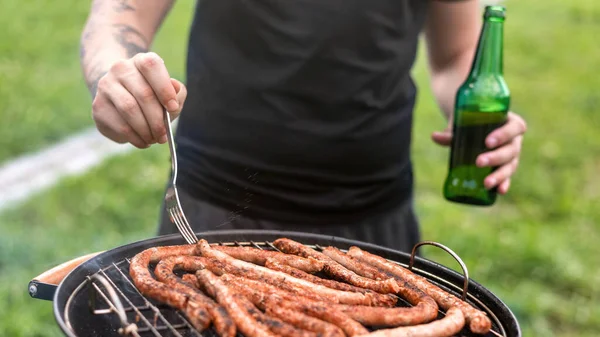 Młody Człowiek Smaży Mięso Grillu Piwo Dłoni Wokół Zieleń Mocowanie — Zdjęcie stockowe