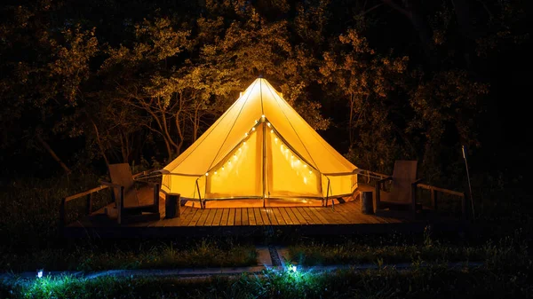 Geceleri glamping, önünde sandalyeler olan parlayan çadır, gece lambaları.