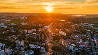 Chisinau şehir merkezindeki hava aracı görüntüsü. Birden fazla bina ve yol manzaralı. Yeşillik yemyeşil, tepeler arka planda, göller. Gün batımı. Moldova