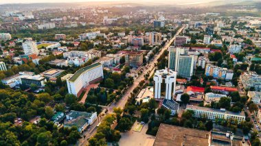Chisinau şehir merkezindeki hava aracı görüntüsü. Birden fazla binanın manzarası, Parlamento, Başkanlık, hareketli arabalı yollar ve gür ağaçlar. Gün batımı. Moldova