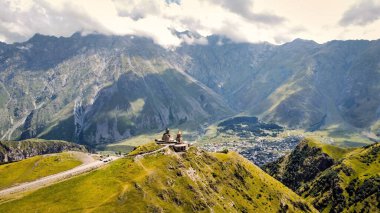 Georgia 'daki doğanın insansız hava aracı görüntüsü. Kafkasya Dağları, Gergeti Trinity Kilisesi bir tepenin, yeşilliğin, vadinin, köyün arka planında yer alır.