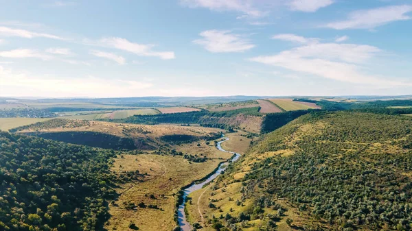 Aerial drone view of a valley with floating river, hill slopes covered with forest, fields and plains in Moldova