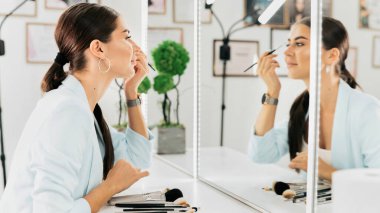 Kadın güzellik salonundaki aynaya bakarak kaşlarını boyuyor.