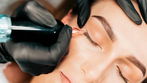 Make-up master performs the procedure of permanent eyebrow makeup for the client