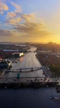 Güneş doğarken Kopenhag 'ın kanallarını ve köprülerini gösteren hava aracı görüntüsü, şehri ve limanı aydınlatan altın ışıkla birlikte. Dikey