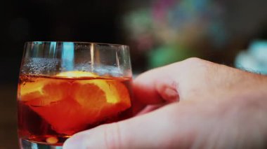 Bar tezgahında bir bardak Negroni kokteyli tutan bir adam.