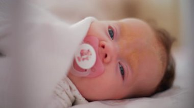 Beyaz bir battaniyenin altında emzik taşıyan bir bebeğe hafifçe yaklaş