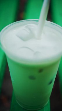 Yeşil bir park bankında bir bardakta karıştırılan buzlu bir kibritin yakın çekimi. Dikey