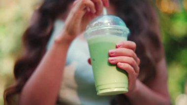 Parkta buzlu kibrit yudumlayan zarif genç bir kadın.