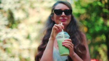 Parkta, güneş ışığında buzlu kibrit içen bir kadının yakın çekimi.