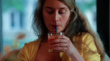 Rahat bir kadın rahat bir kafede pipetten meyve suyu yudumluyor.