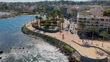 Antibes 'in deniz manzaralı insansız hava aracı, palmiye ağaçlarıyla kaplı kıvrımlı yürüyüş yolu, Akdeniz ve modern şehir binalarına bakan