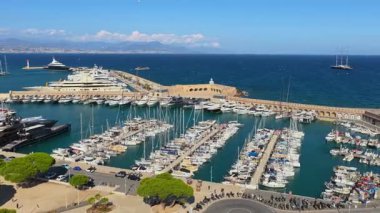 Antibes, Fransa - 4 Eylül 2025: Süper yatları ve yelkenlileri kenetlenmiş uzun taş dalgakıranları ve ötesindeki derin mavi Akdeniz ile limanın insansız hava aracı görüntüsü