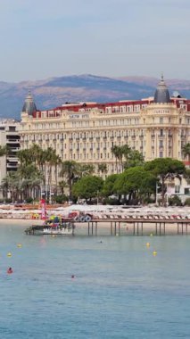 Cannes, Fransa - 6 Eylül 2025: İnsanların kumsalda dinlendiği ve turkuaz denizde yüzdüğü, palmiye ağaçları ve şehir binalarıyla çevrili havadan insansız hava aracı görüntüsü