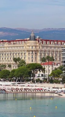 Cannes, Fransa - 6 Eylül 2025: İnsanların kumsalda dinlendiği ve turkuaz denizde yüzdüğü, palmiye ağaçları ve şehir binalarıyla çevrili havadan insansız hava aracı görüntüsü