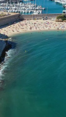 Antibes kumsalının güneşlenenlerle, turkuaz sularla ve lüks yatları olan marinalarla dolu insansız hava aracı manzarası. Dikey