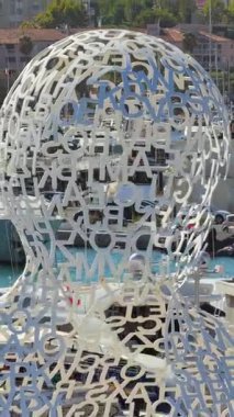 Antibes, Fransa - 4 Eylül 2025: Antibes 'te Jaume Plensa' nın Nomade heykelinin havadan drone görüntüsü, arka planda yatlar ve lüks tekneler. Dikey