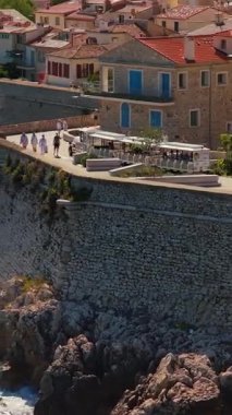 Antibes, Fransa - 4 Eylül 2025: Antibes 'in taştan surları ve kayalık Akdeniz kıyılarına tepeden bakan ziyaretçilerle birlikte deniz kenarına bakan hava aracı görüntüsü. Dikey