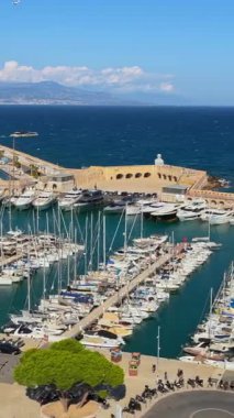 Antibes, Fransa - 4 Eylül 2025: Limana yanaşmış süper yatlar ve yelkenliler, uzun taş dalgakıranlar ve ötesindeki derin mavi Akdeniz 'in hava aracı görüntüsü. Dikey