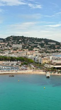 Cannes sahil şeridinin havadan insansız hava aracı görüntüsü, marina, sahil önü ve yamaçtaki konut binaları. Dikey