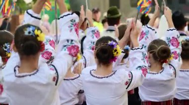 Nakışlı giysiler giyen bir grup dansçı, canlı bir kültür festivalinde geleneksel halk dansını zevkle icra ediyor.