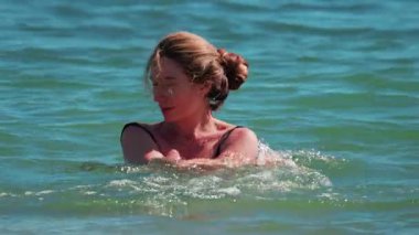 Turkuvaz deniz suyunda yüzen kadın, güneş ışığının ve huzurlu çevrenin tadını çıkarıyor.