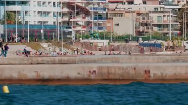 Cannes, Fransa - 6 Ekim 2025: İnsanlar yürürken ve yakınlarda dinlenirken modern bir tren sahilin kıyısından geçiyor