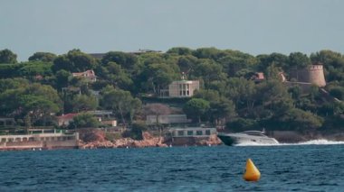 Yeşil çam ağaçlarıyla çevrili güzel villalarla dolu bir yat sahil boyunca ilerliyor.