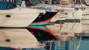 Bir marinaya demirlemiş birkaç yatın yakınında, sakin sularda gövdelerinin canlı yansımaları var.