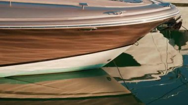 Bir yatın pruvasına yakın sıcak güneş ışığı altında parıldıyor, parlak şekli durgun yeşil suyun üzerinde güzel bir şekilde yansıyor.