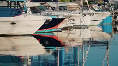 Bir marinaya demirlemiş birkaç yatın yakınında, sakin sularda gövdelerinin canlı yansımaları var.