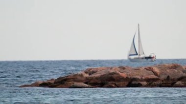 Kayalık kıyı oluşumlarının gerisinde bir yelkenli süzülüyor.