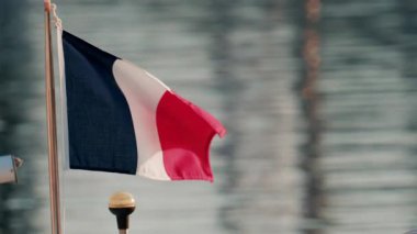 Fransız bayrağı, arka planda denizin yansımasıyla küçük bir gemi direğinde dalgalanıyor.