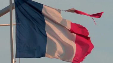 Açık mavi gökyüzünün altında rüzgarda zarif bir şekilde dalgalanan Fransız ulusal bayrağının yakın çekimi