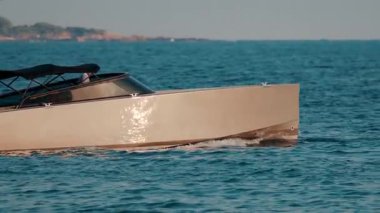 Pürüzsüz bir bej tekne, sakin mavi sularda süzülür. Gövdesinden yansıyan güneş ışığıyla.