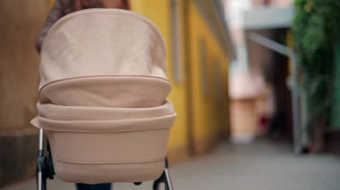 Sarı ve kahverengi duvarları olan dar bir sokakta ilerleyen bej bebek arabasının arka görüntüsü.