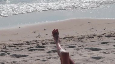 Sahilde uzanan bir kadının bacakları nazikçe dalgalanır.