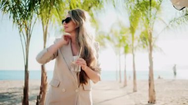 Palmiye ağaçlarının altındaki plaj barında dinlenirken elinde bir bardak limon suyu tutan zarif bir kadın.