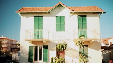 Yeşil kepenkleri ve açık mavi gökyüzünün altında kırmızı kiremitli çatısı olan büyüleyici bir Akdeniz tarzı evin ön görüntüsü