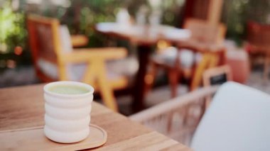 Beyaz seramik bir fincan yeşil kibrit sütlü latte. Açık hava kafesinde, ahşap bir masada.
