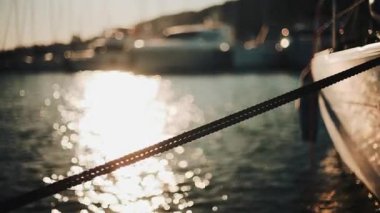 Altın güneş ışığı, sakin bir suda yüzen bir yatın kenarında parıldıyor.